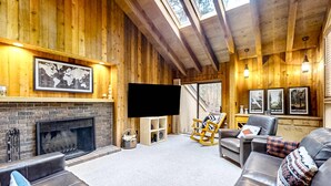Un salon chaleureux avec une cheminée, des canapés en cuir, des murs en bois et un grand téléviseur.