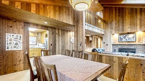 Un intérieur en bois comprenant une table à manger, des chaises, un luminaire suspendu et un coin cuisine.