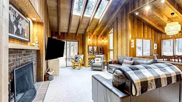 L’intérieur d’une cabane en rondins, avec une cheminée, un coin salon et de grandes fenêtres.