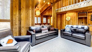 Un intérieur en bois avec un canapé et un fauteuil, un coin repas et un plafond avec des poutres apparentes.