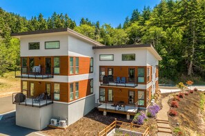 Una casa moderna de dos pisos con balcones, ventanas amplias y un jardín ajardinado.