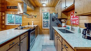 Eine Holzhütte mit einer Küche, ausgestattet mit einer Edelstahl-Dunstabzugshaube, einem Kühlschrank, einer Spüle und einer Kaffeemaschine.