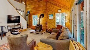 Ein Holzinnenraum mit einer Couch, einem Fernseher, einem Kamin und einer Treppe.