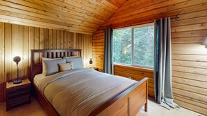Ein Schlafzimmer einer Holzhütte mit einem Bett, Nachttischen und einem Fenster mit Vorhängen.