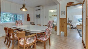 Uma sala de jantar com mesa branca, cadeiras de madeira e uma poltrona estampada.