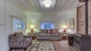 Uma sala de estar com sofá, poltrona estampada, tapete, lareira e janela com cortinas.