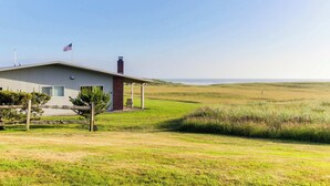 A modern house with a covered porch, a flag, and a grassy field in the background. - Oceanfront getaway close to Gearhart Golf Links , no pets (Gearhart)