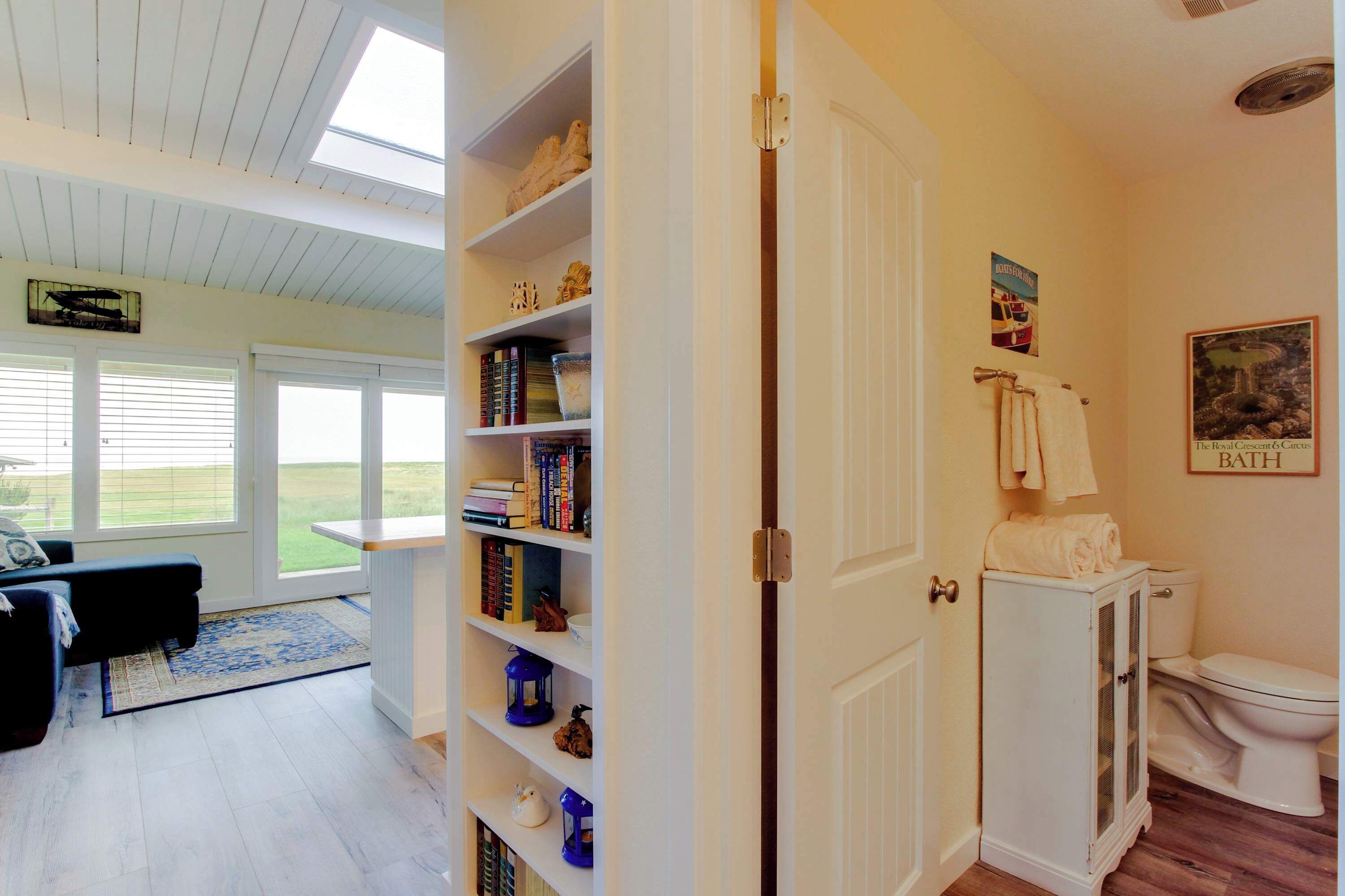 Ein Zimmer mit Bücherregal, einem weißen Schrank, einer Toilette und einem Fenster mit Blick auf ein grünes Feld.