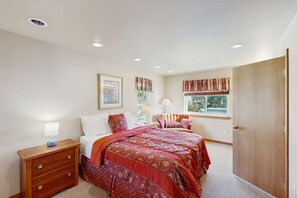 A bedroom with a bed, bedside table, lamp, window with curtains, and a door.
