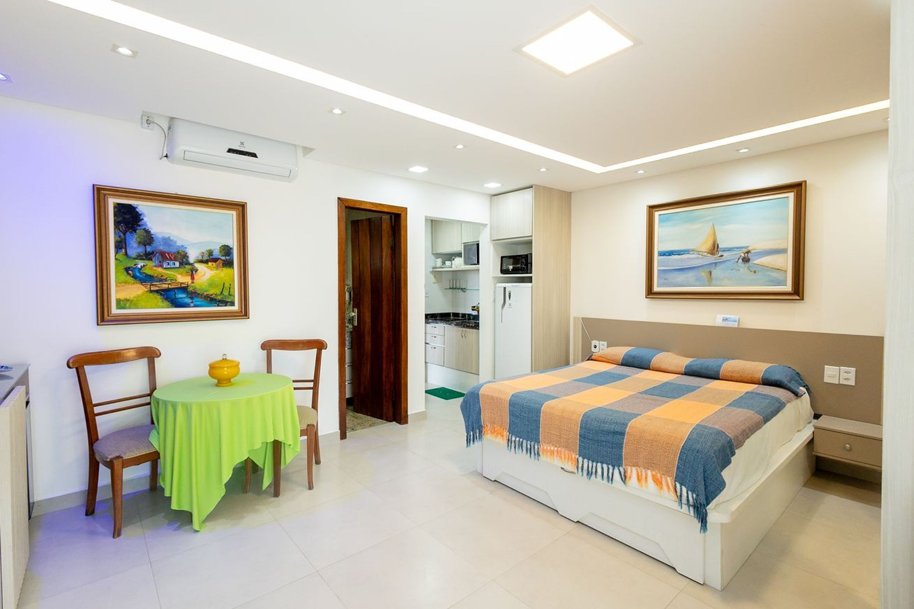 Una camera da letto con un letto, un tavolo con sedie, un quadro appeso al muro e un angolo cottura sullo sfondo.