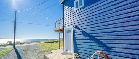 Ein blaues Haus mit einer Veranda, Stufen zum Eingang und einem Gartenschlauch an der Seite.