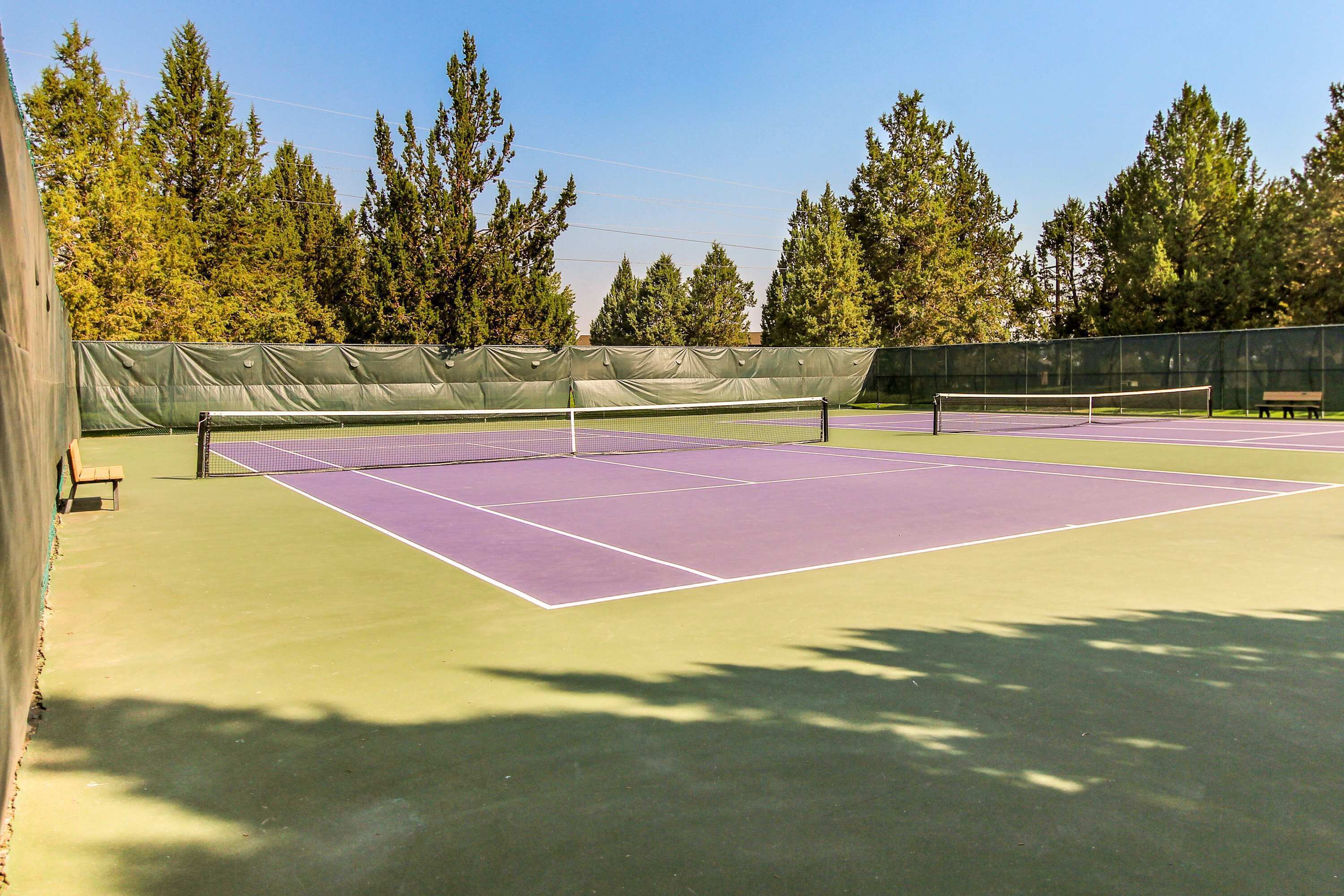 A tennis court with a net, surrounded by trees and a fence.