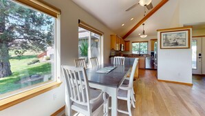 A dining area with a long table and white chairs, a ceiling fan, and a view of the outdoors. - Charming waterfront townhouse with fireplace, pool, hot tub, & washerdryer (Eagle Crest)