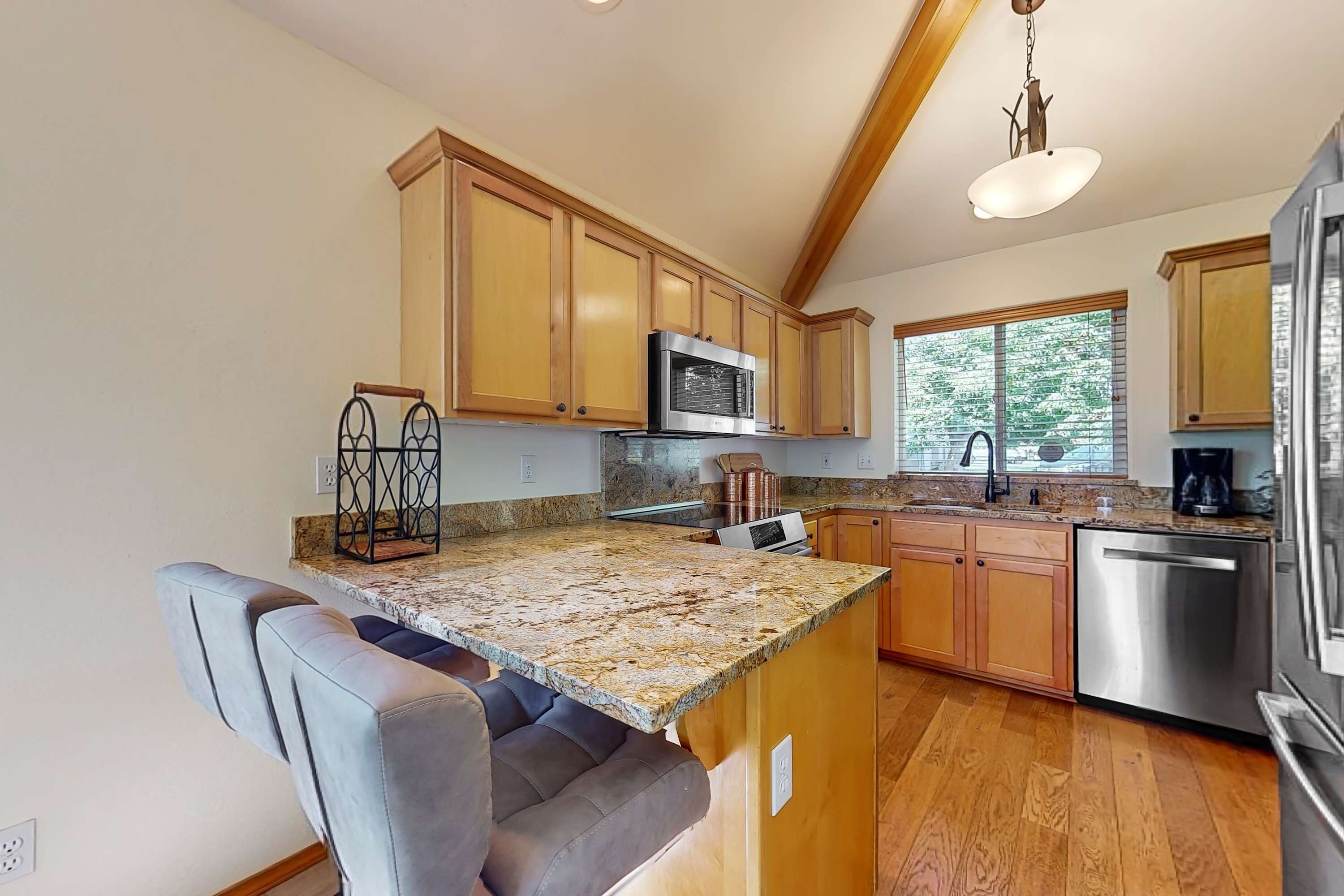 A kitchen with wooden cabinets, a granite countertop, a built-in microwave, a stainless steel dishwasher, and a window providing natural light.