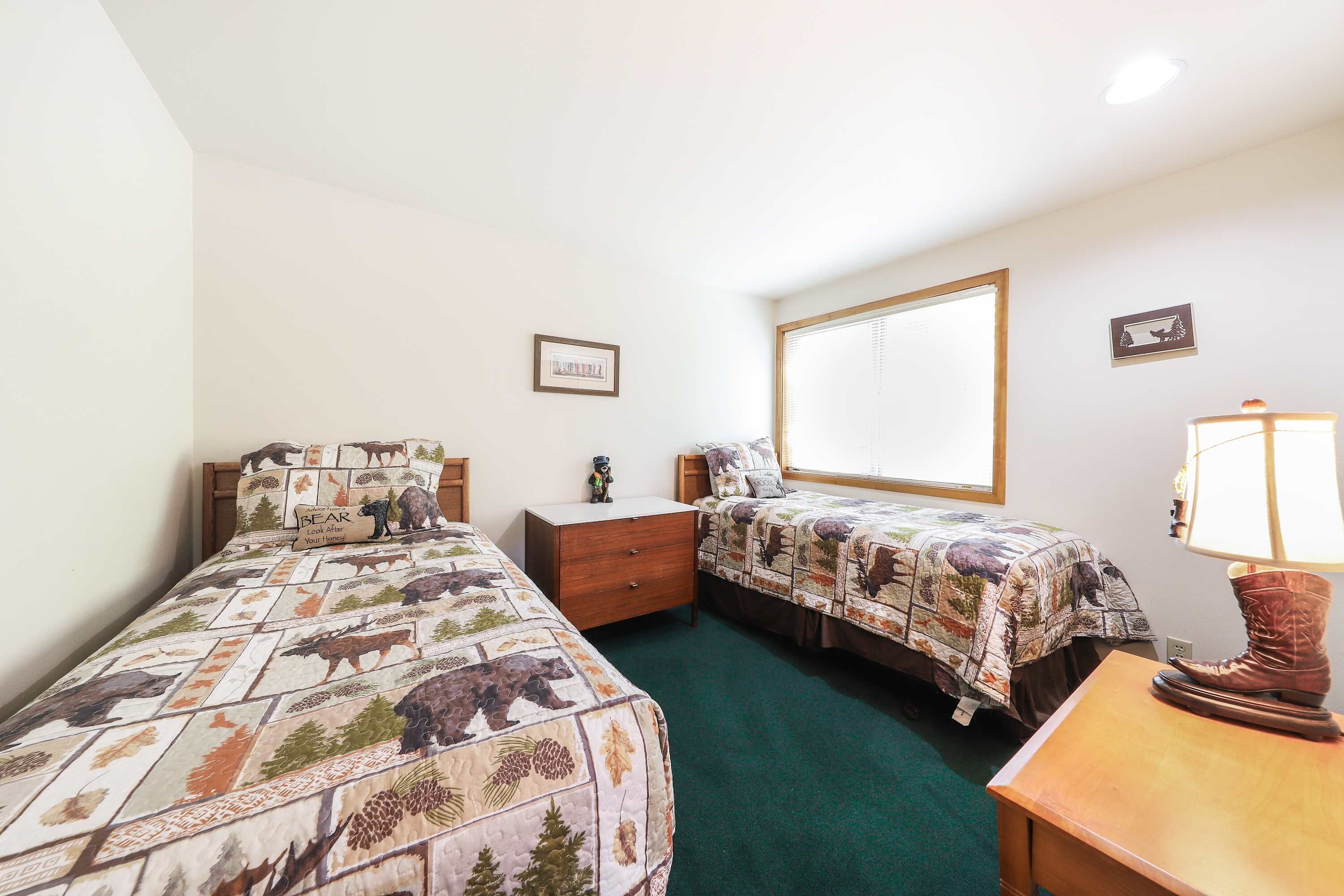 A bedroom with two beds, a nightstand, a lamp, and a window with blinds.