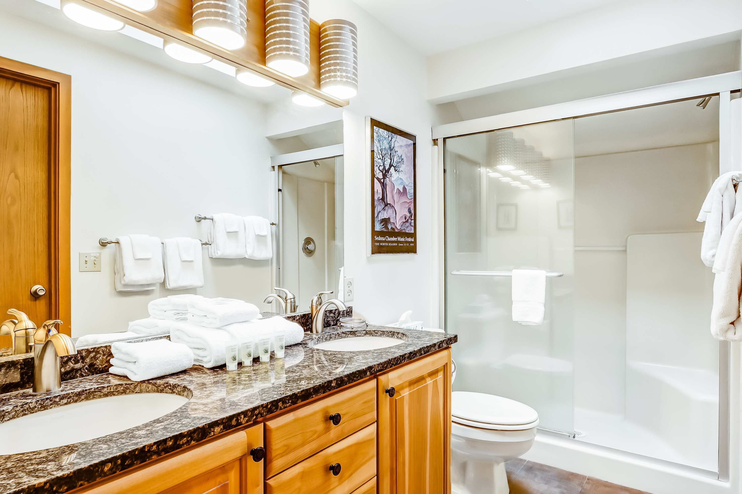 A modern bathroom with a marble sink, wooden cabinets, a large mirror, and a glass shower enclosure.