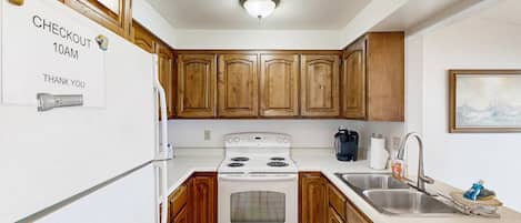 A kitchen with wooden cabinets, a white refrigerator, a stove, and a sink.