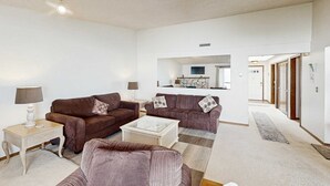 Ein Wohnzimmer mit zwei braunen Sofas, einem Glastisch, einem gestreiften Sessel und einer weißen Lampe auf einem Beistelltisch.