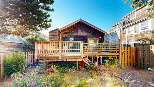 A wooden cabin with a deck, surrounded by a fenced yard with vegetation.
