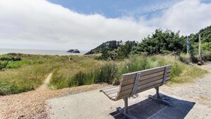 A bench on a concrete path with a view of the ocean and a grassy hill.