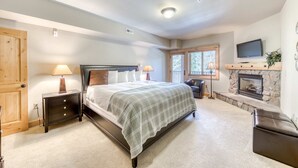 A bedroom with a bed, bedside lamps, a wooden nightstand, a fireplace, and a television. - Lovely mountain condo with shared pool, hot tub, sauna & balcony views & free WiFi (Government Camp)