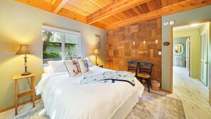 Una camera da letto con soffitto in legno, un letto con copriletto a tema nautico, una finestra vista verde e una sedia.