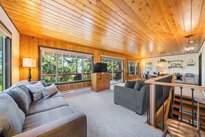 A spacious living room with a wooden ceiling, a sofa, a TV, and a staircase. - Hidden Oasis - House in Manzanita with 3 decks, walk to the beach (Manzanita)
