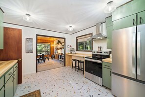 A kitchen with a large stove, a refrigerator, and a dining area with chairs and a table. - Hidden Oasis - House in Manzanita with 3 decks, walk to the beach (Manzanita)