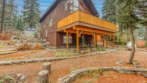 A wooden cabin with a wooden deck, surrounded by trees and a stone wall. - Dog-Friendly, 3-Story Home & Loft with Deck, Private Hot Tub, Gas Grill, Pool Table (Government Camp)