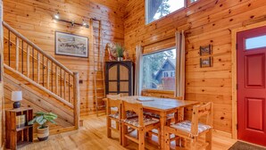 A wooden interior with a staircase, a dining table with chairs, a red door, and a window with a view of a house outside. - Dog-Friendly, 3-Story Home & Loft with Deck, Private Hot Tub, Gas Grill, Pool Table (Government Camp)