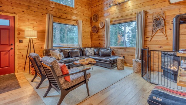 A cozy cabin interior with a wooden interior, a sofa, chairs, a table, and a fireplace. - Dog-Friendly, 3-Story Home & Loft with Deck, Private Hot Tub, Gas Grill, Pool Table (Government Camp)