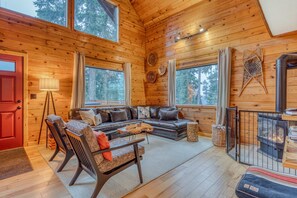 Interior acogedor de una cabaña con detalles de madera, un sofá, sillas, una mesa y una chimenea.