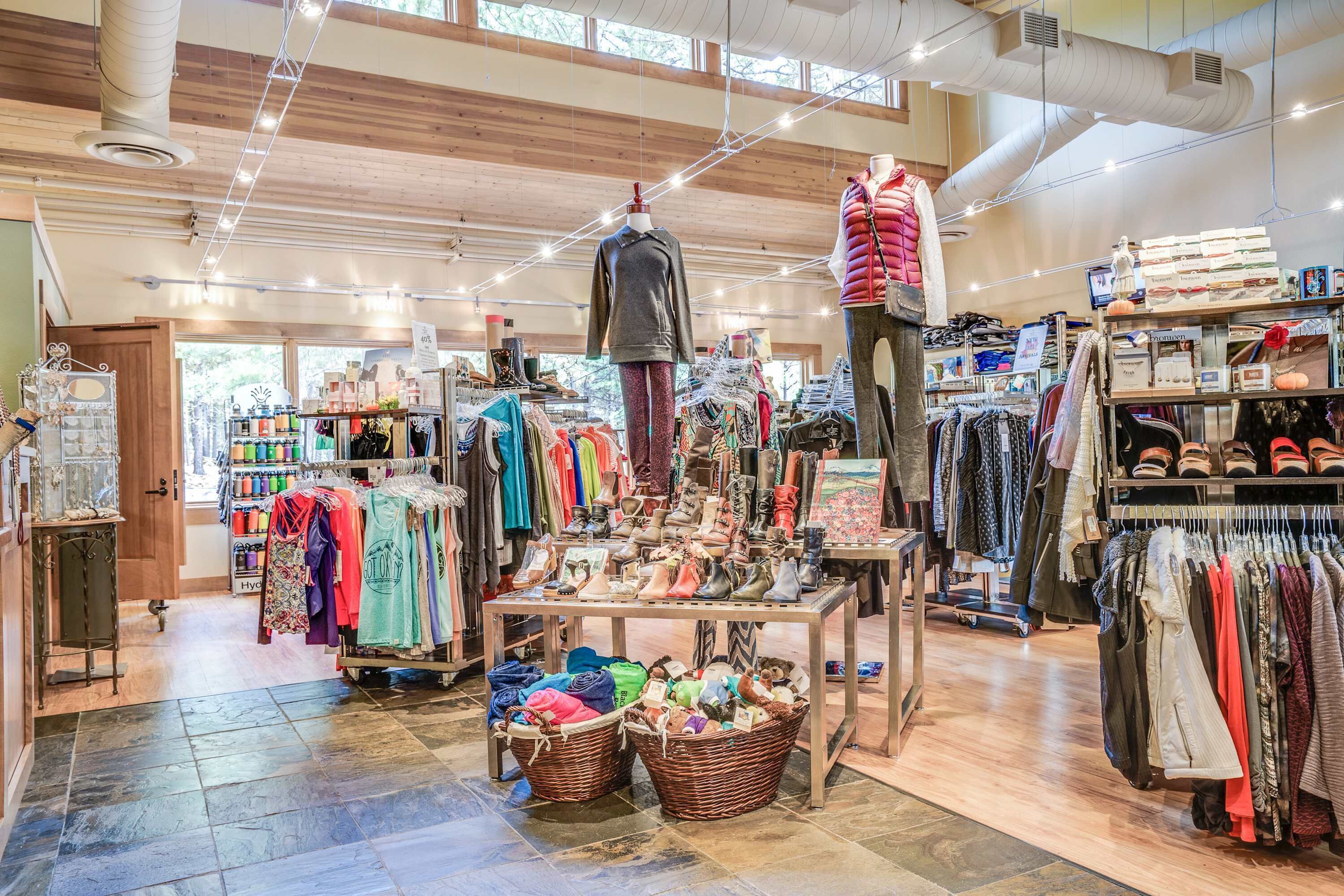 Un magasin de vêtements avec des portants remplis de vêtements, une table de présentation avec des chaussures et un mannequin.