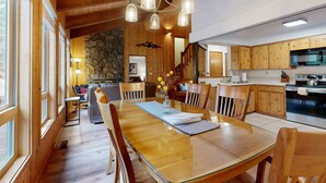 Een houten interieur met een eettafel, stoelen, een kroonluchter en een keukenhoek.