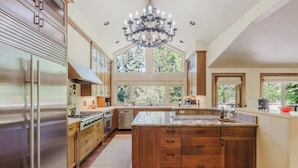 A spacious kitchen with a large island, stainless steel appliances, wooden cabinets, and a chandelier. - Lovely home with pool, hot tub, balcony, & washer/dryer (Sunriver)