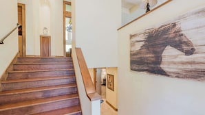 A wooden staircase with a handrail, a wall-mounted lamp, and a large abstract horse painting. - Lovely home with pool, hot tub, balcony, & washer/dryer (Sunriver)