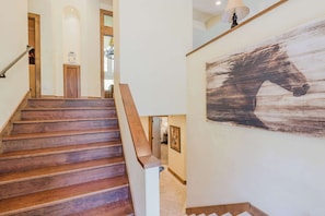 Eine Holztreppe mit Handlauf, einer Wandleuchte und einem großen, abstrakten Gemälde eines Pferdes.