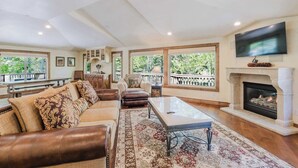 A spacious living room with a fireplace, leather sofa, and a large TV. - Lovely home with pool, hot tub, balcony, & washer/dryer (Sunriver)