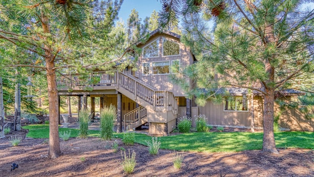 A two-story house with a deck, surrounded by pine trees. - Lovely home with pool, hot tub, balcony, & washer/dryer (Sunriver)