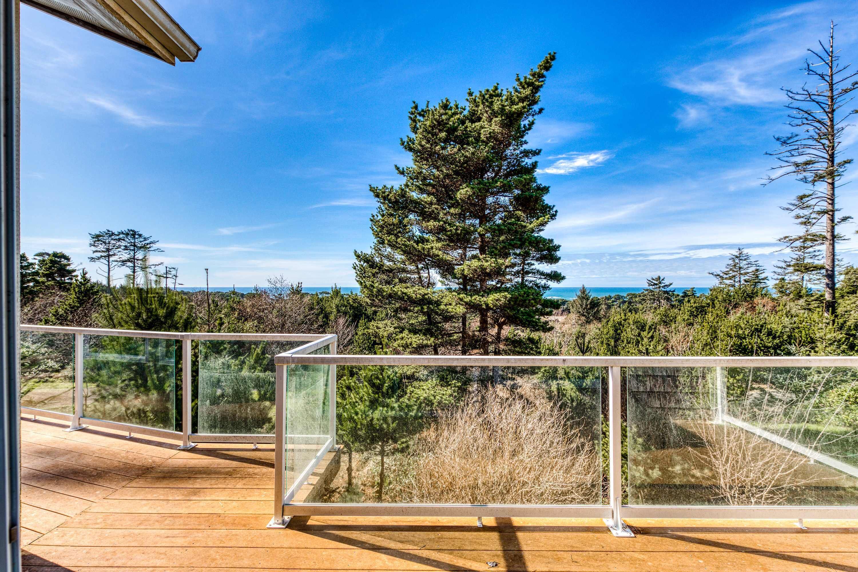 A wooden deck with glass railings overlooking a forested area and a clear sky.
