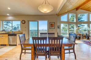 Un coin repas avec une table et des chaises en bois, une cuisine équipée d’un lave-vaisselle et de grandes fenêtres offrant une vue dégagée.