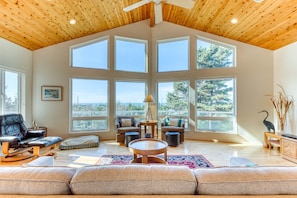 A spacious living room with a high ceiling, large windows, and a view of the outdoors.