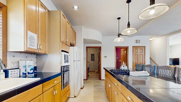 A kitchen with wooden cabinets, a black countertop, a stove, and overhead lighting. - Large home 1 block from the beach with ocean view, game room, fireplace & WiFi (Seaside)