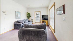 A living room with a sofa, a television, and a window with blinds. - Large home 1 block from the beach with ocean view, game room, fireplace & WiFi (Seaside)