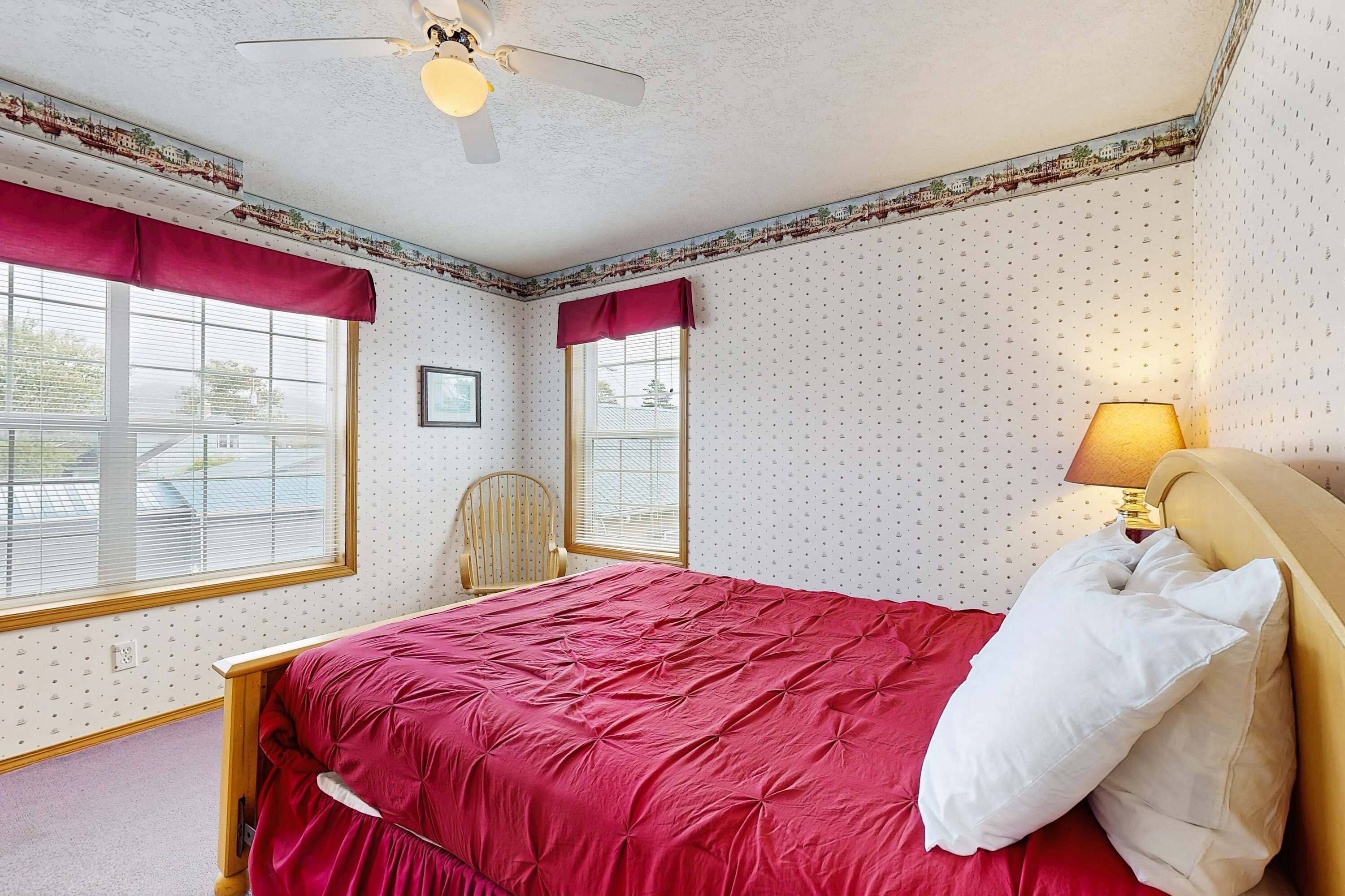 A bedroom with a bed, a chair, a ceiling fan, and a window with blinds.