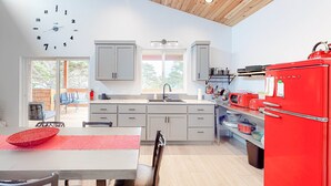 A modern kitchen with a red refrigerator, white cabinets, a clock, and a dining area with a red placemat. - Beachy, Dog-Friendly Home Near the Coast with Free WiFi & a Kitchenette (Bandon)