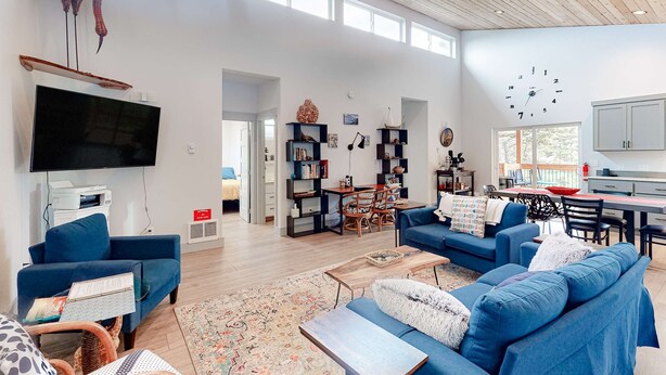 A spacious living area with a large flat-screen TV, blue sofas, a dining table, and a kitchen area. - Beachy, Dog-Friendly Home Near the Coast with Free WiFi & a Kitchenette (Bandon)