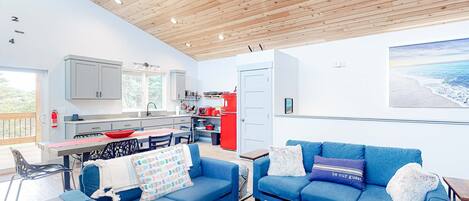 Una sala de estar moderna con un sofá azul, una mesa de centro de madera y una cocina al fondo.