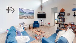 A spacious living room with a blue sofa, a coffee table, a TV, and a bookshelf. - Beachy, Dog-Friendly Home Near the Coast with Free WiFi & a Kitchenette (Bandon)