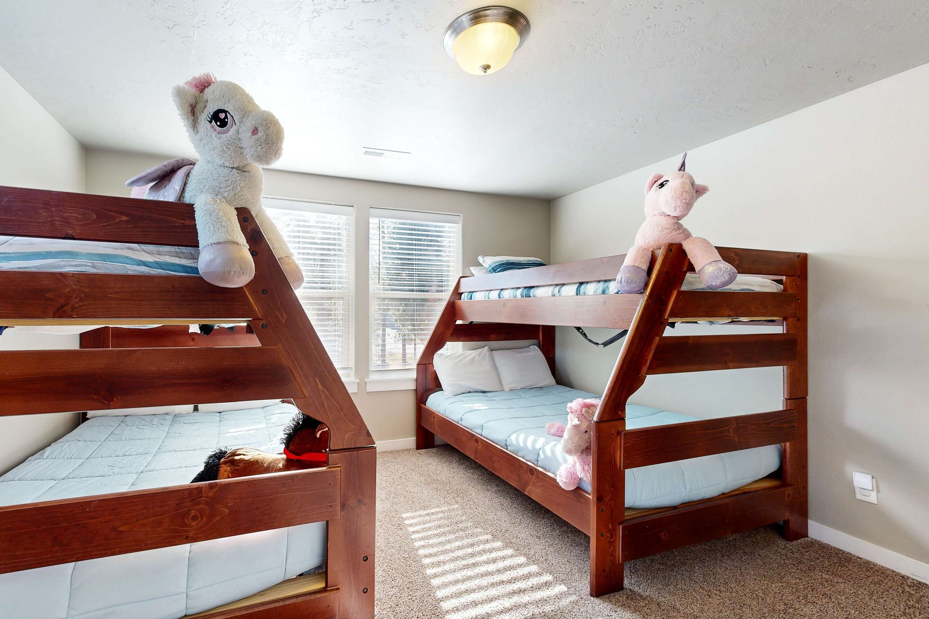 Two bunk beds with plush toys, a window with blinds, and a ceiling light fixture.